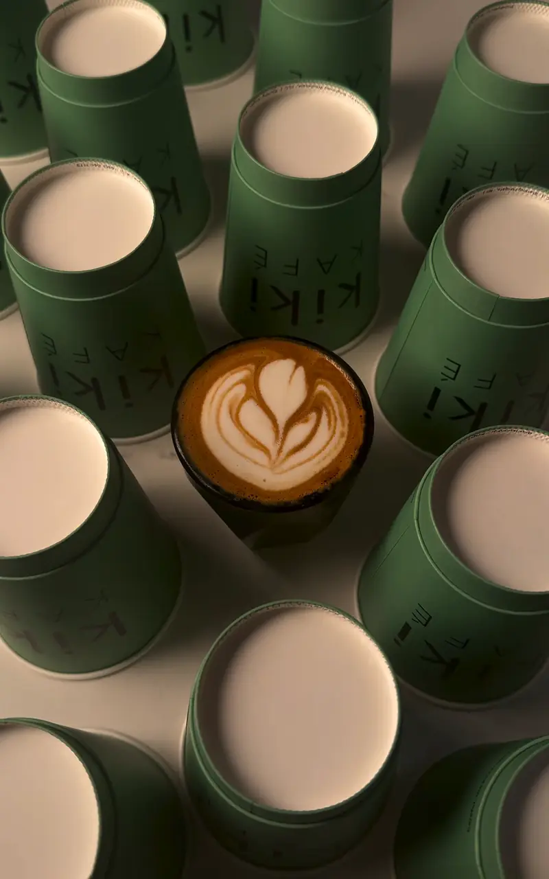 Cortado with latte art among green Kiki Kafé cups